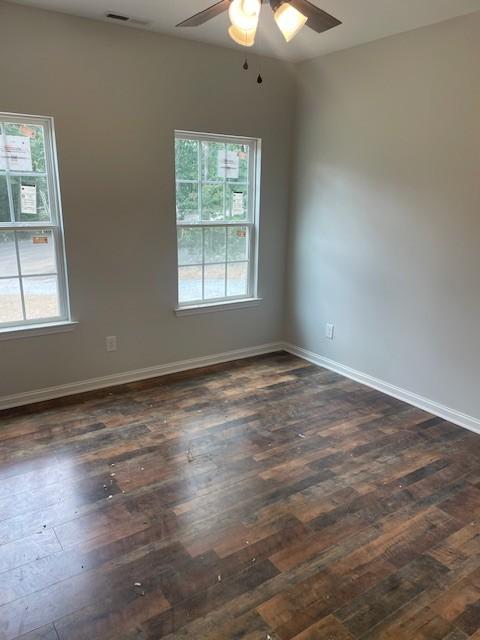 empty room featuring a healthy amount of sunlight, ceiling fan, and dark wood-type flooring