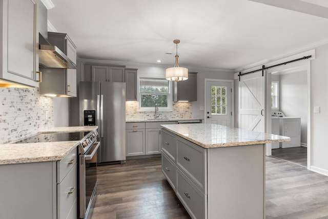 kitchen featuring sink, stainless steel appliances, washing machine and dryer, decorative light fixtures, and a barn door