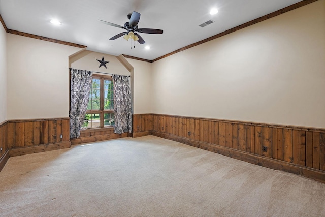 empty room featuring ceiling fan, carpet flooring, wooden walls, and crown molding