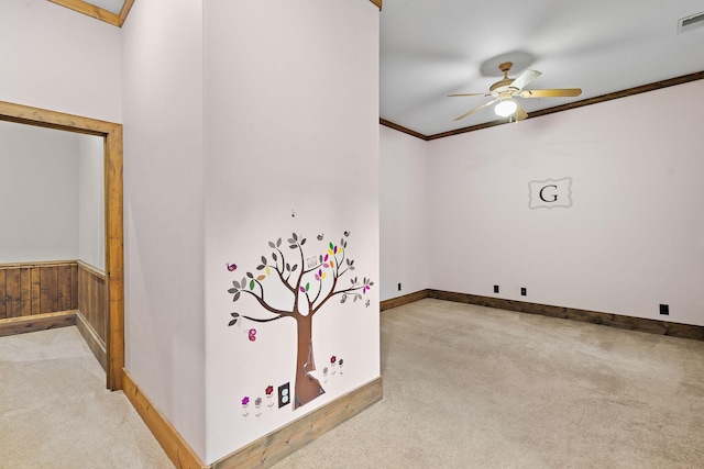 spare room featuring crown molding, light carpet, ceiling fan, and wood walls