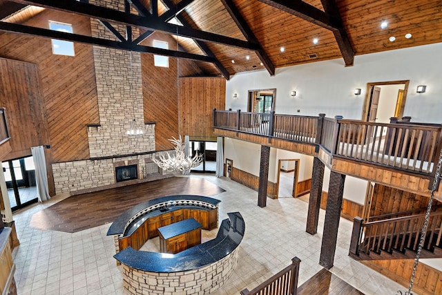 living room with wood ceiling, beam ceiling, wooden walls, high vaulted ceiling, and an outdoor fireplace