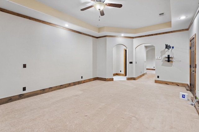 empty room with a tray ceiling, light colored carpet, and ceiling fan