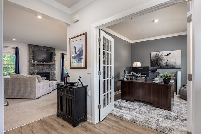 office space with ornamental molding, light hardwood / wood-style flooring, a stone fireplace, and french doors