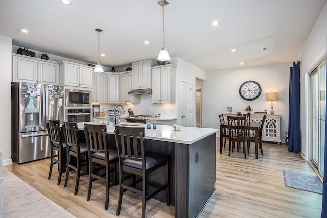 kitchen with light wood-type flooring, stainless steel appliances, a kitchen breakfast bar, decorative light fixtures, and a center island with sink