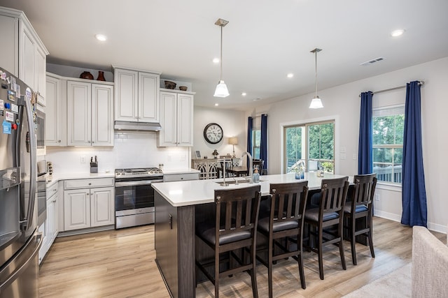 kitchen with stainless steel gas range oven, tasteful backsplash, a kitchen island with sink, light hardwood / wood-style floors, and sink