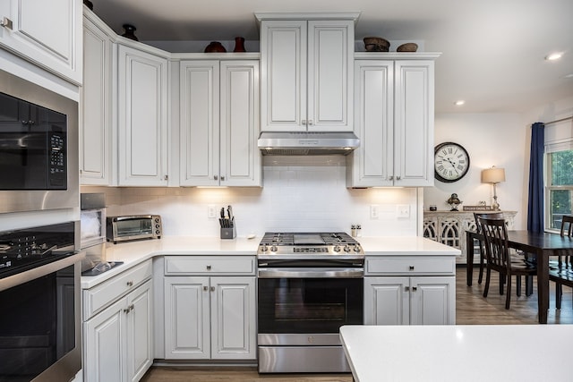 kitchen with appliances with stainless steel finishes, wood-type flooring, backsplash, and white cabinets