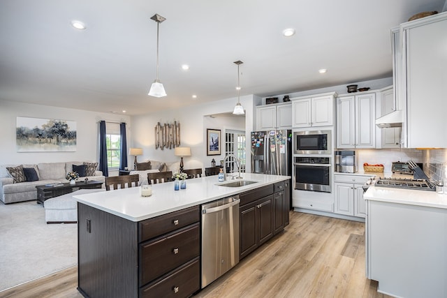 kitchen with white cabinets, a kitchen island with sink, hanging light fixtures, appliances with stainless steel finishes, and light carpet