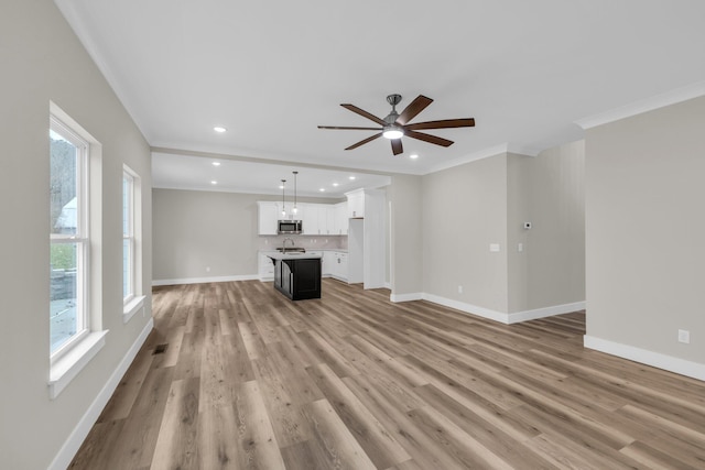 unfurnished living room with light wood-type flooring, ceiling fan, crown molding, and sink