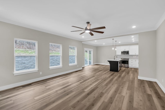 unfurnished living room featuring ornamental molding, sink, ceiling fan, and light wood-type flooring