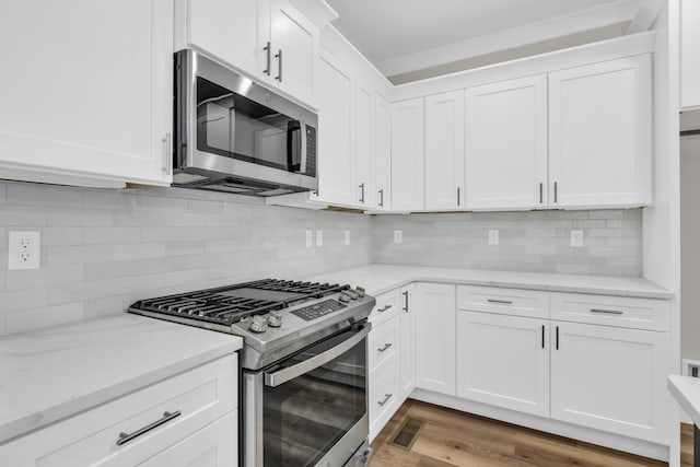 kitchen with white cabinetry, light stone counters, wood-type flooring, appliances with stainless steel finishes, and backsplash