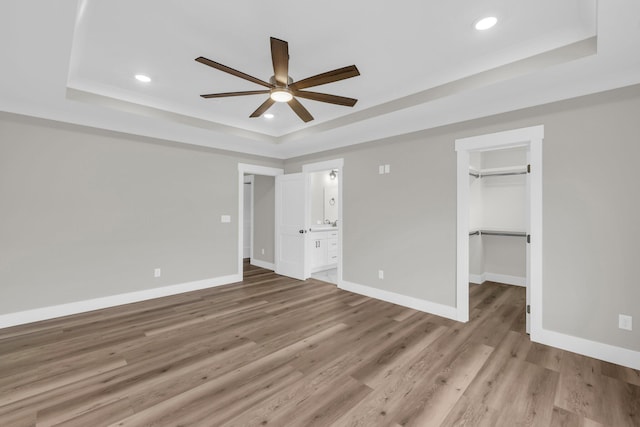 unfurnished bedroom with a tray ceiling, ceiling fan, a spacious closet, light hardwood / wood-style flooring, and a closet