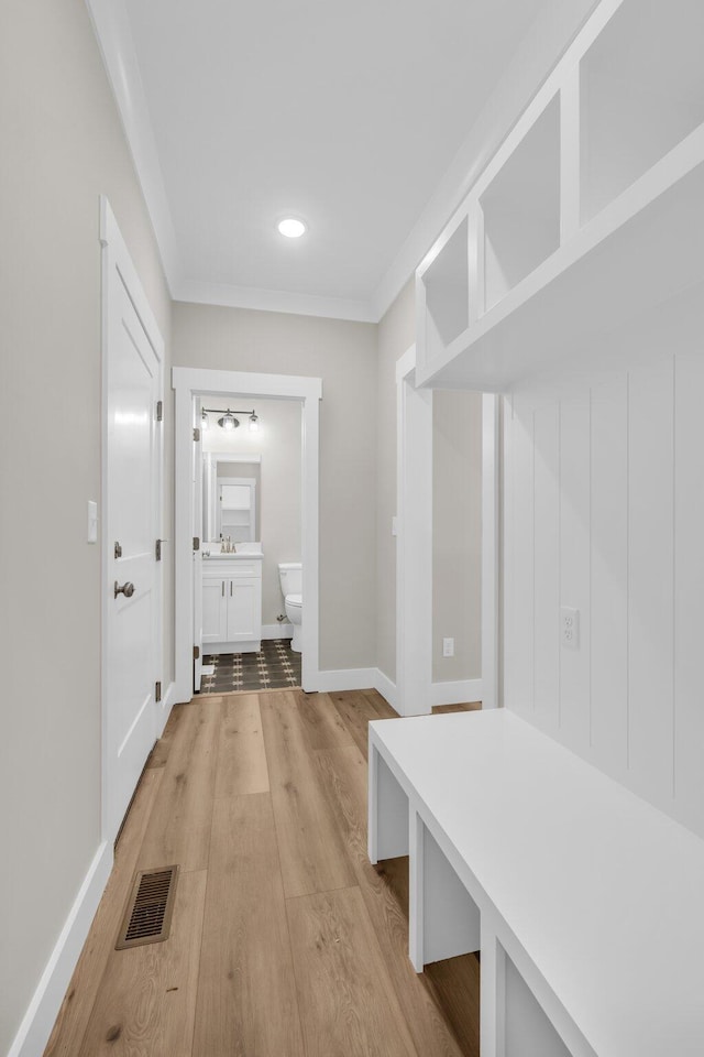 mudroom with crown molding, sink, and light hardwood / wood-style flooring