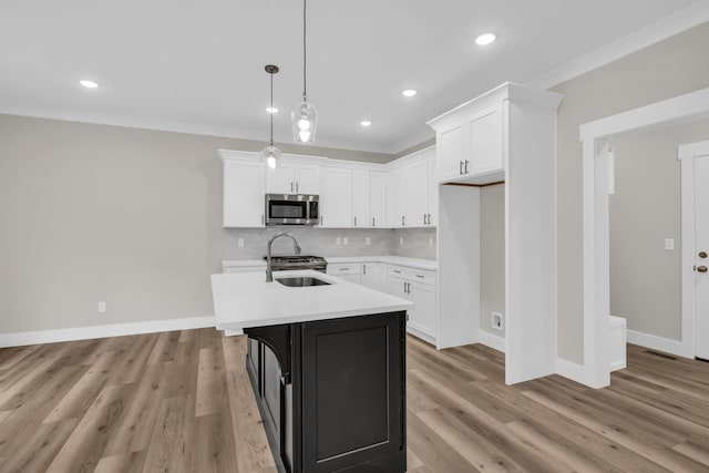 kitchen with white cabinetry, stainless steel appliances, crown molding, decorative light fixtures, and a center island with sink