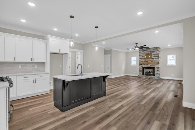 kitchen featuring pendant lighting, sink, a fireplace, an island with sink, and white cabinetry