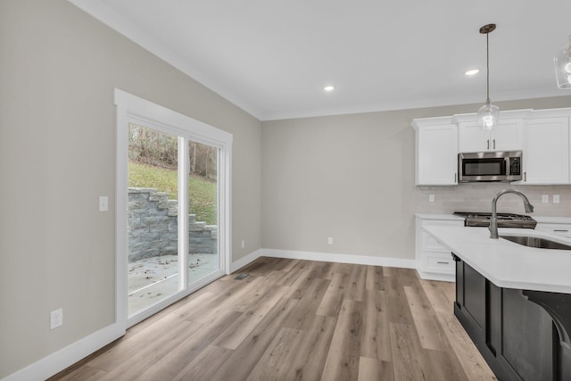 kitchen featuring sink, light hardwood / wood-style flooring, white cabinets, pendant lighting, and backsplash