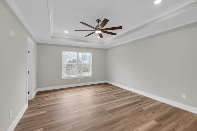 empty room with a tray ceiling, ceiling fan, and light hardwood / wood-style floors