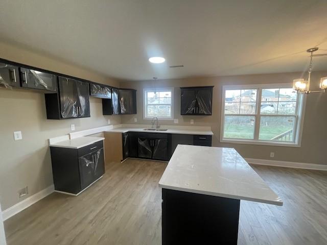 kitchen with pendant lighting, a center island, sink, light wood-type flooring, and a chandelier