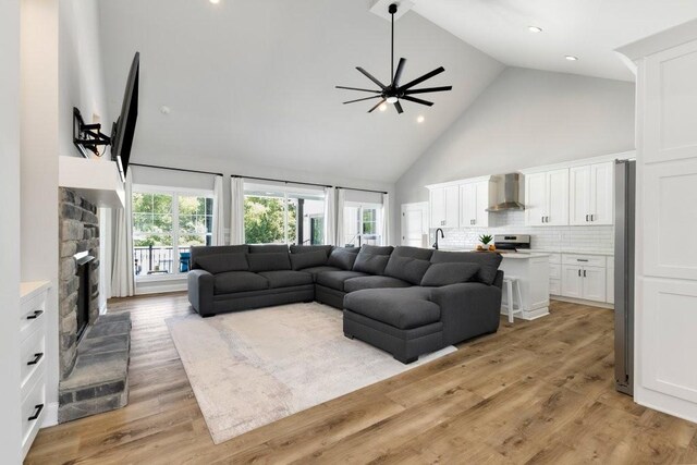 living room featuring ceiling fan, high vaulted ceiling, a fireplace, light hardwood / wood-style floors, and sink