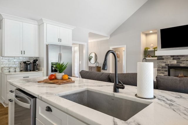 kitchen featuring appliances with stainless steel finishes, hardwood / wood-style flooring, light stone countertops, a brick fireplace, and vaulted ceiling