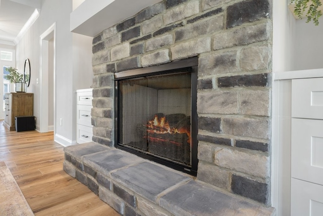 interior details featuring wood-type flooring, a stone fireplace, and ornamental molding