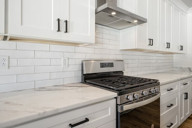 kitchen featuring decorative backsplash, light stone counters, gas stove, white cabinets, and wall chimney exhaust hood