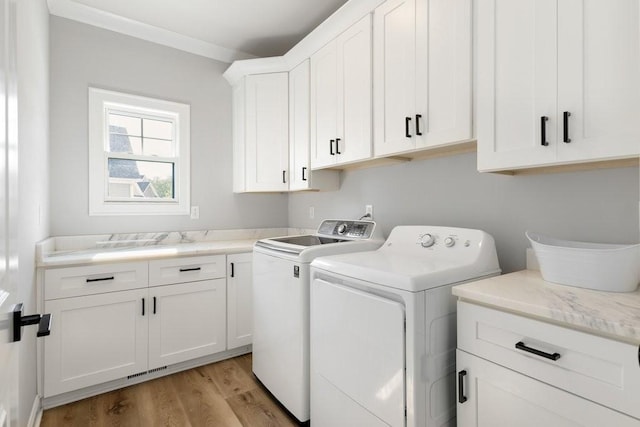 clothes washing area featuring separate washer and dryer, ornamental molding, light hardwood / wood-style floors, and cabinets