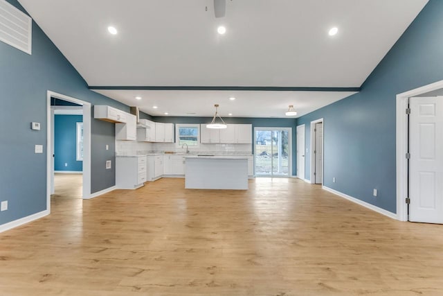 kitchen featuring hanging light fixtures, a center island, light hardwood / wood-style floors, white cabinets, and decorative backsplash