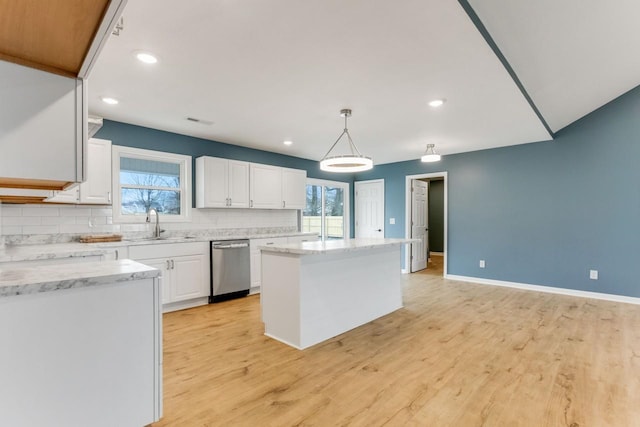 kitchen with a wealth of natural light, a kitchen island, decorative light fixtures, stainless steel dishwasher, and white cabinets