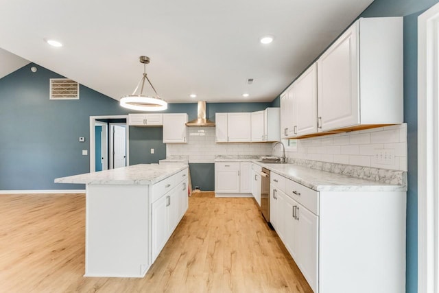 kitchen with white cabinetry, hanging light fixtures, a kitchen island, sink, and wall chimney exhaust hood