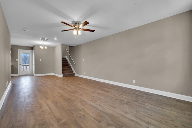 spare room featuring ceiling fan with notable chandelier, wood finished floors, visible vents, baseboards, and stairs