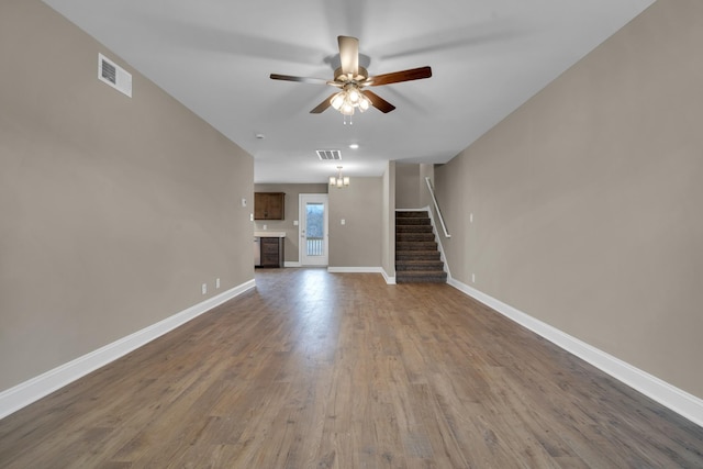 unfurnished living room with ceiling fan, visible vents, baseboards, stairway, and dark wood-style floors