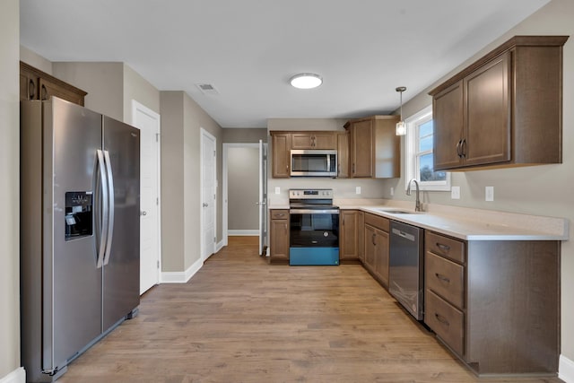 kitchen with stainless steel appliances, a sink, visible vents, light countertops, and light wood finished floors