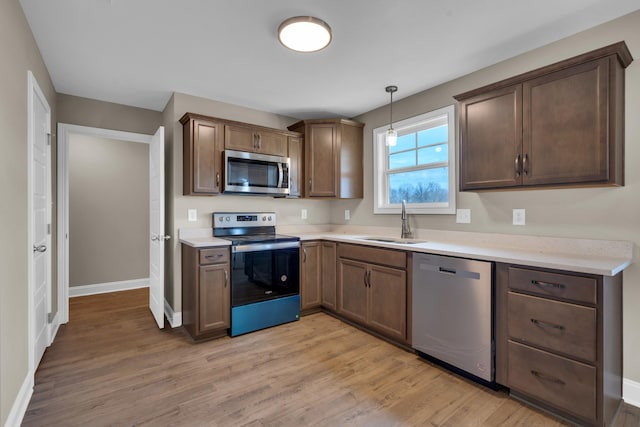 kitchen featuring light countertops, appliances with stainless steel finishes, a sink, light wood-type flooring, and baseboards