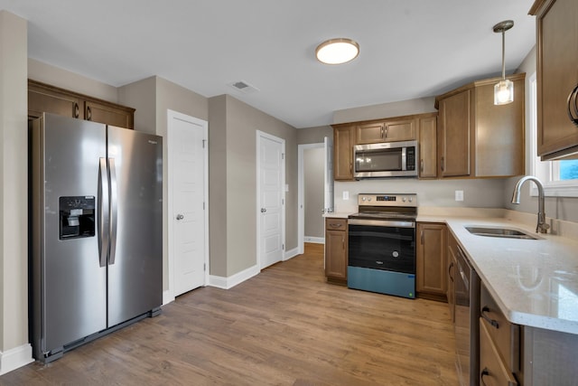 kitchen with light wood-type flooring, pendant lighting, stainless steel appliances, and a sink