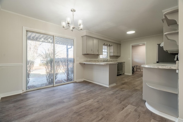 kitchen with an inviting chandelier, pendant lighting, kitchen peninsula, gray cabinets, and hardwood / wood-style flooring