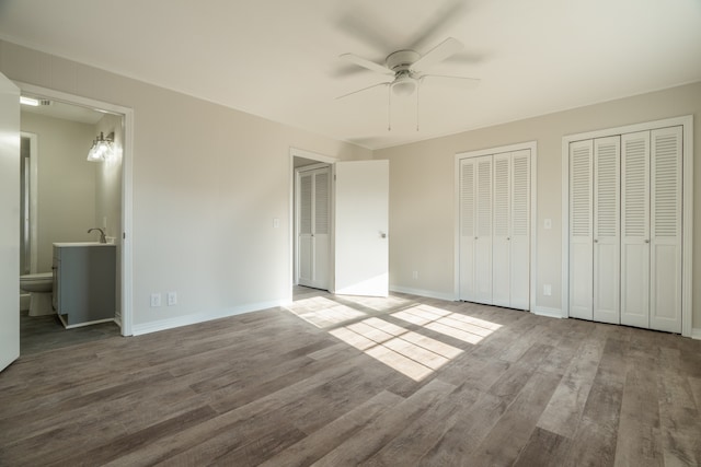 unfurnished bedroom with ceiling fan, hardwood / wood-style floors, ensuite bathroom, multiple closets, and sink