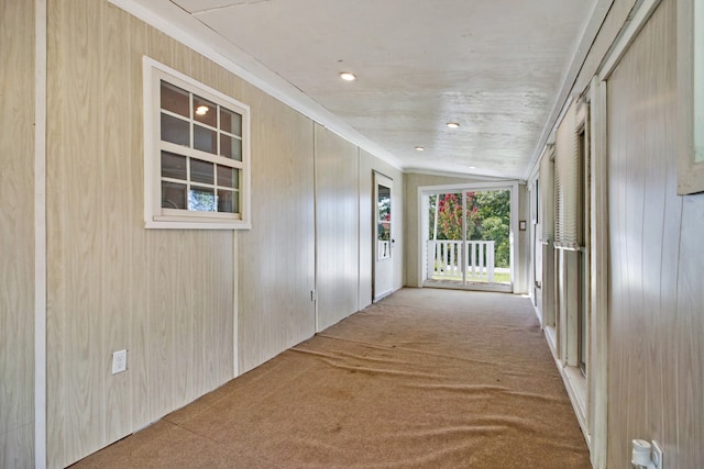 hall with light colored carpet, wooden walls, and vaulted ceiling