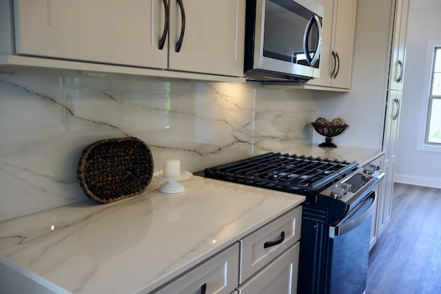 kitchen with appliances with stainless steel finishes, decorative backsplash, light wood-type flooring, and light stone countertops