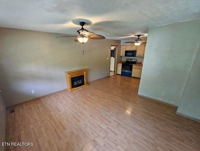 unfurnished living room featuring ceiling fan, a fireplace, light wood finished floors, and a textured ceiling