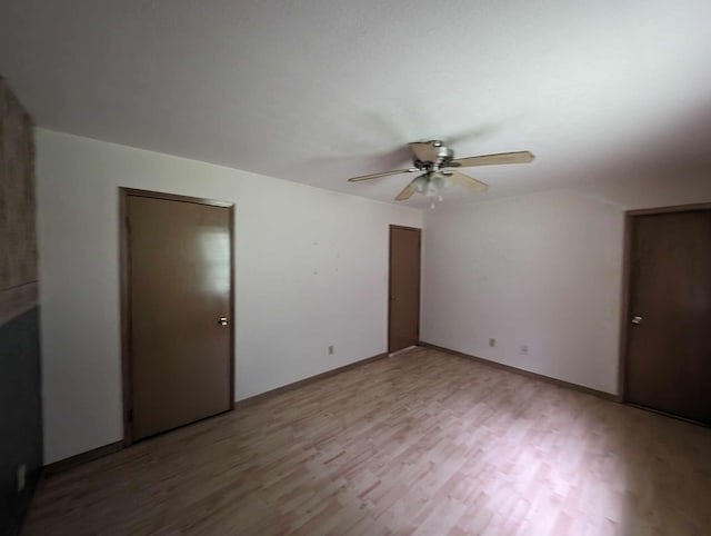 unfurnished bedroom with baseboards, multiple closets, wood finished floors, and a ceiling fan