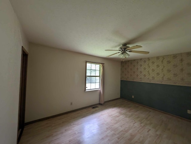 spare room featuring a textured ceiling, light wood-style floors, wallpapered walls, baseboards, and ceiling fan