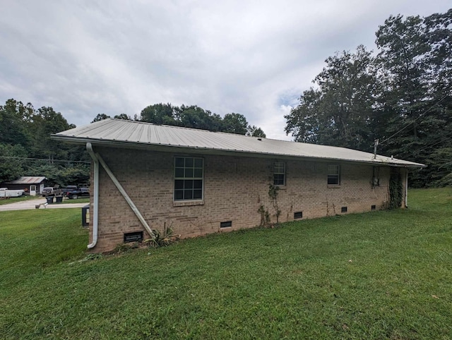 rear view of house featuring crawl space, brick siding, a yard, and metal roof