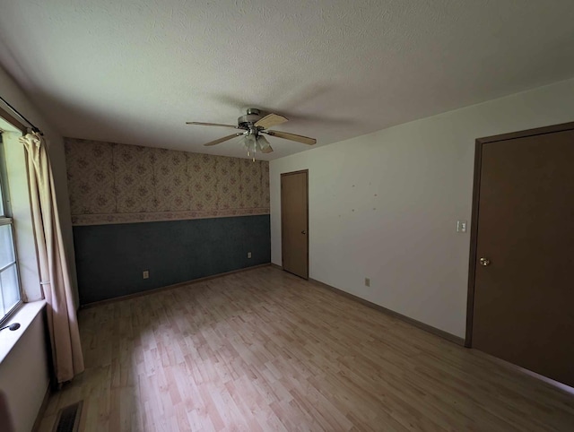 empty room featuring visible vents, a textured ceiling, wallpapered walls, and light wood-style floors