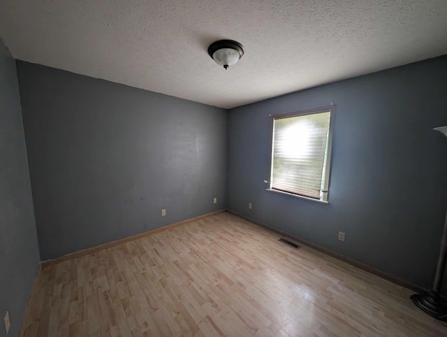 empty room with visible vents, baseboards, a textured ceiling, and wood finished floors