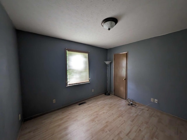 empty room featuring visible vents, light wood-style floors, and a textured ceiling