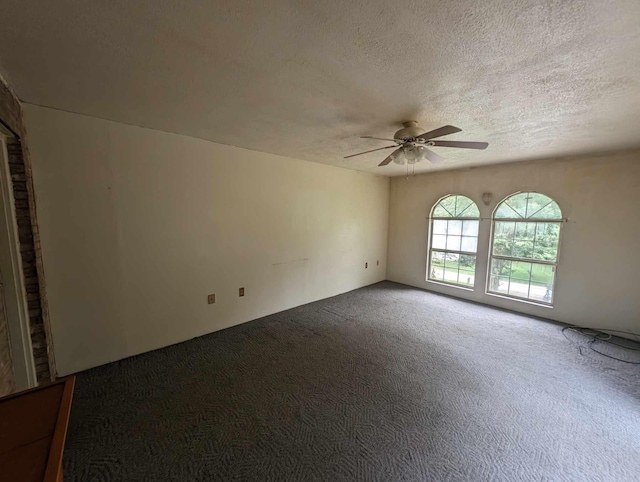 empty room featuring ceiling fan, dark colored carpet, and a textured ceiling