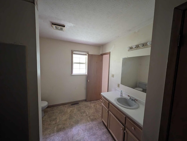 bathroom with visible vents, baseboards, toilet, vanity, and a textured ceiling