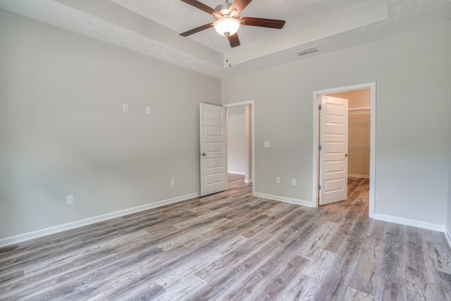 unfurnished bedroom featuring ceiling fan, a tray ceiling, light hardwood / wood-style floors, a textured ceiling, and a spacious closet