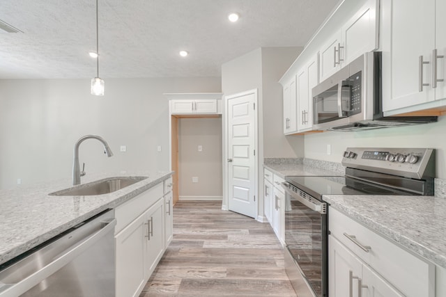 kitchen with pendant lighting, sink, stainless steel appliances, light stone counters, and white cabinets