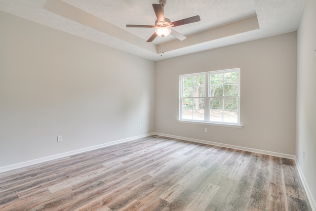 empty room featuring ceiling fan, a tray ceiling, a textured ceiling, and light wood-type flooring